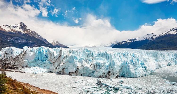 Un glacier massif entouré de montagnes sous un ciel bleu.