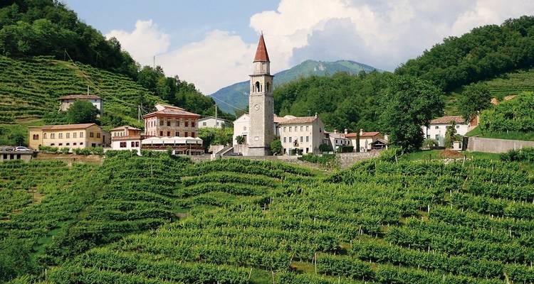 A scenic view of a church in a village surrounded by lush green hills.