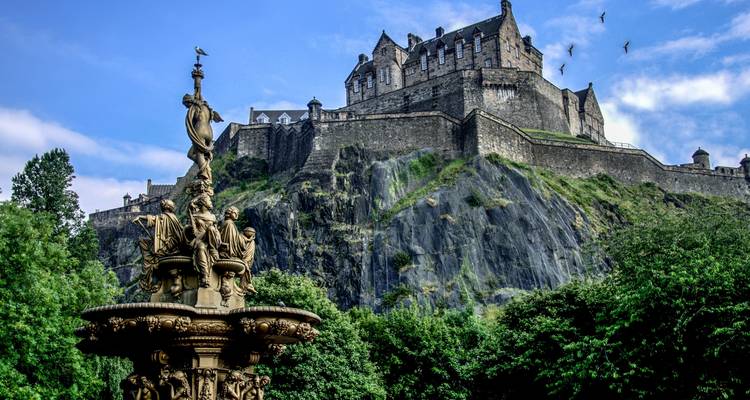 Château d'Édimbourg sur une colline rocheuse avec une statue.