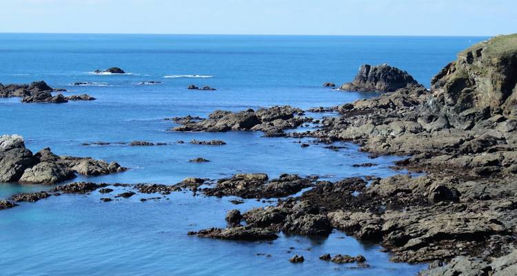 Rocky shoreline with small waves and blue ocean waters.