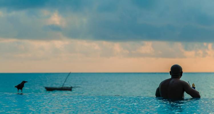 A person in a pool overlooking the ocean during sunset.