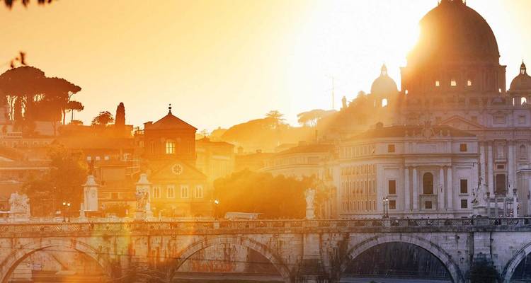 El amanecer naranja resplandece detrás de la Basílica de San Pedro y el Ponte Sant'Angelo que cruza el río Tíber.