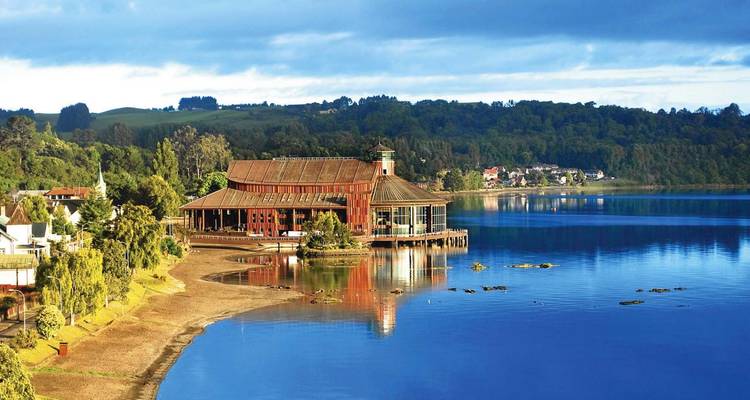 Gebouw aan het meer met beboste heuvels op de achtergrond.