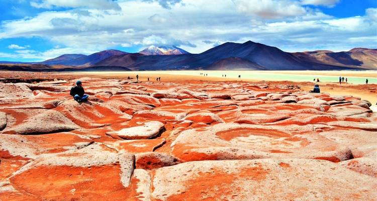 Toeristen lopen op een levendig oranje woestijnlandschap.