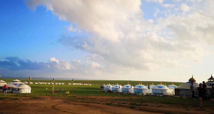 Yurts in een grasrijke vlakte onder een bewolkte hemel.