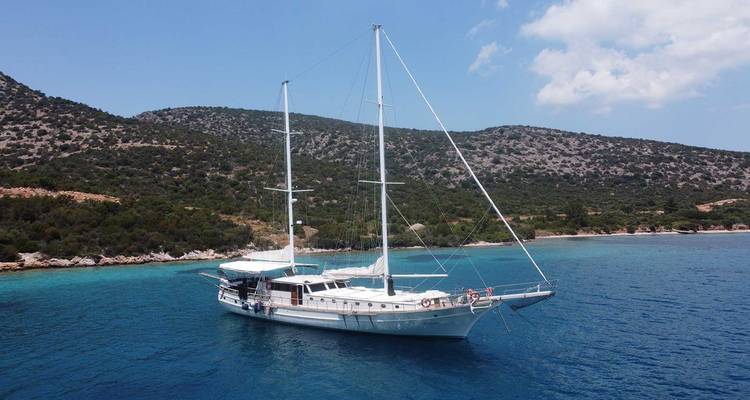 Voilier ancré dans une baie tranquille avec des collines en arrière-plan.