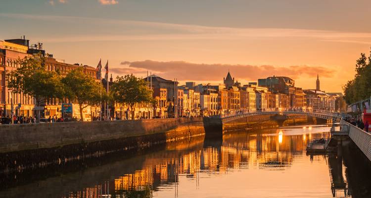 Sonnenuntergangsblick auf eine Stadtlandschaft mit einem Fluss und einer historischen Brücke.