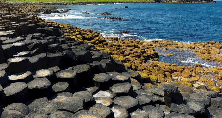 Sechseckige Basaltsäulen des Giant's Causeway treffen auf leuchtend blaue Atlantikwellen.