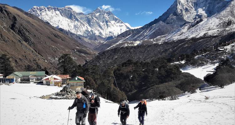 Quatre randonneurs marchant sur un sentier enneigé avec des montagnes enneigées au loin.