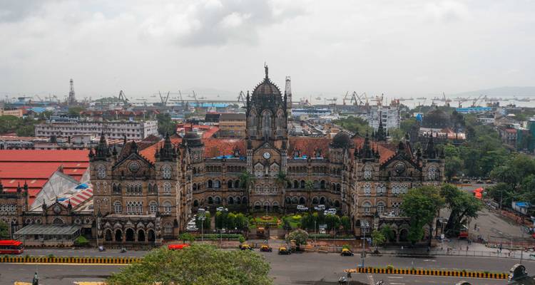 Estación de tren histórica en un entorno urbano con puerto en el fondo.