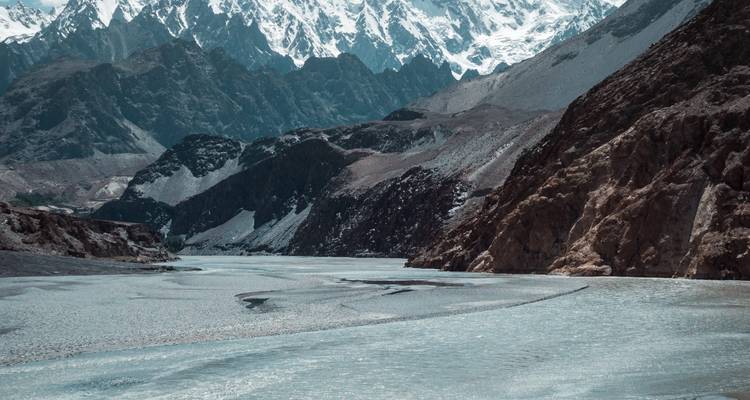 Ijzige blauwe rivier die slingert door een dramatisch hooggelegen dal omringd door ruige, sneeuwbedekte toppen.