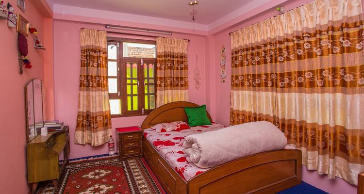Colorful homestay bedroom with pink walls, patterned curtains and a single wooden bed