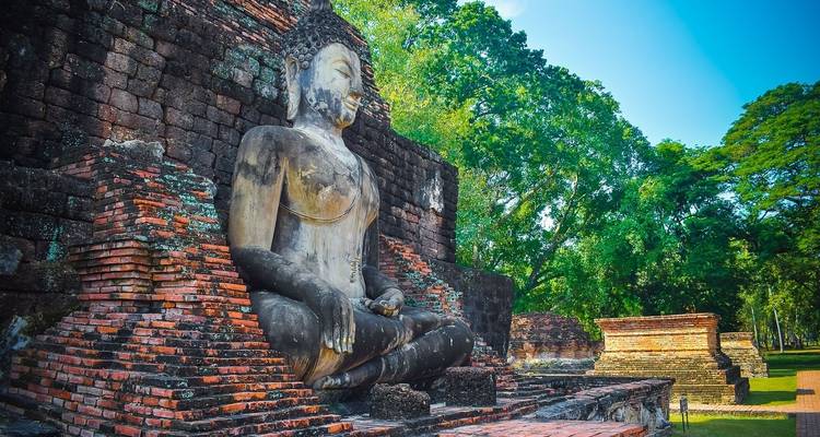 Buddha statue at an ancient brick temple in lush greenery.