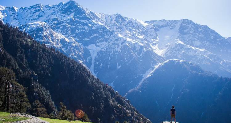 Person, die auf einem Hügel steht und auf schneebedeckte Berge blickt.