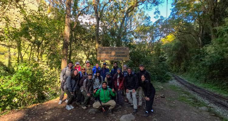 Een groep mensen verzameld voor een houten bord in een bosgebied.