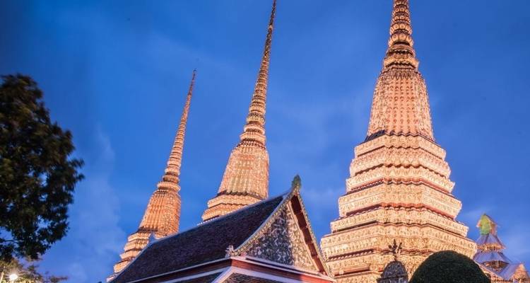 Stupas iluminadas del Wat Pho de Bangkok brillando contra un cielo azul profundo al atardecer.
