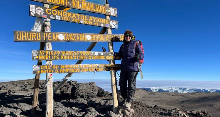 Klimmer staat naast het Uhuru Peak-bord op de met sneeuw bedekte top van de Mount Kilimanjaro.