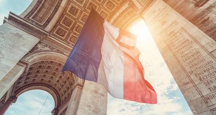 Drapeau français flottant sous l'Arc de Triomphe avec des rayons de soleil qui filtrent.