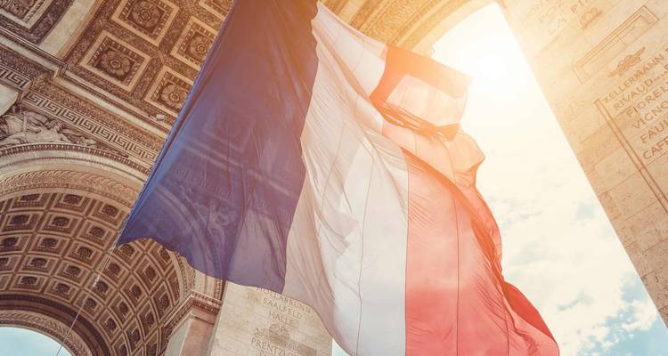 La bandera tricolor francesa ondea bajo el arco de piedra ornamentado del Arco del Triunfo bajo la brillante luz del sol.