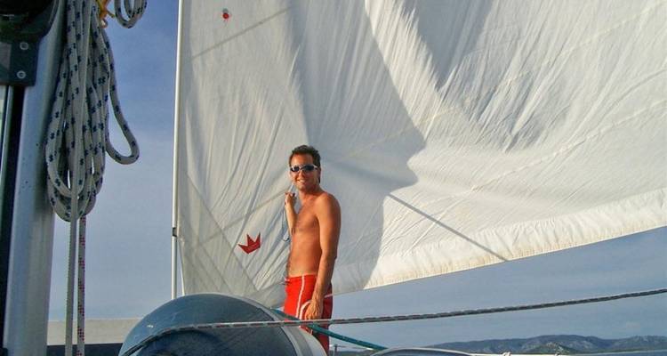 A man on a sailboat standing in front of sails.