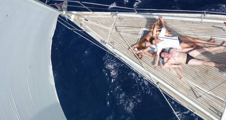 Menschen, die auf dem Deck eines Segelboots entspannen, mit dem Meer im Hintergrund.