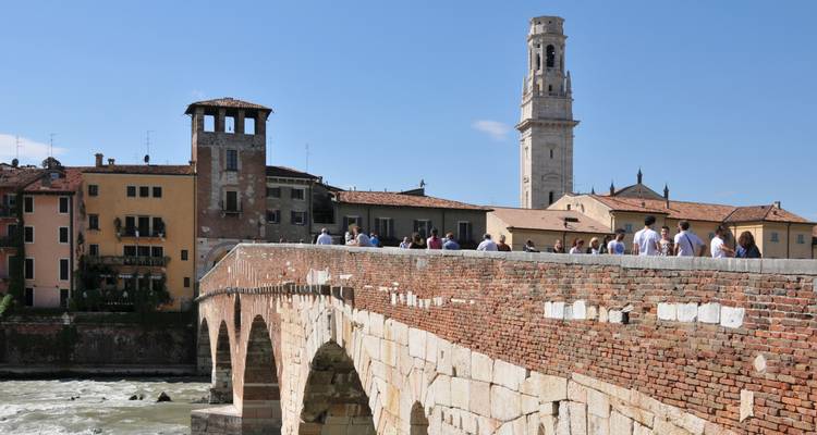 Historic stone bridge Ponte Pietra crosses the Adige River with Verona’s bell tower rising behind.