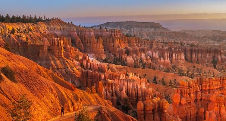 Person walking along the rim of Bryce Canyon at sunset.