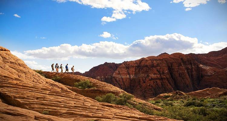 Silhouetted hikers on a red rock formation with blue sky.