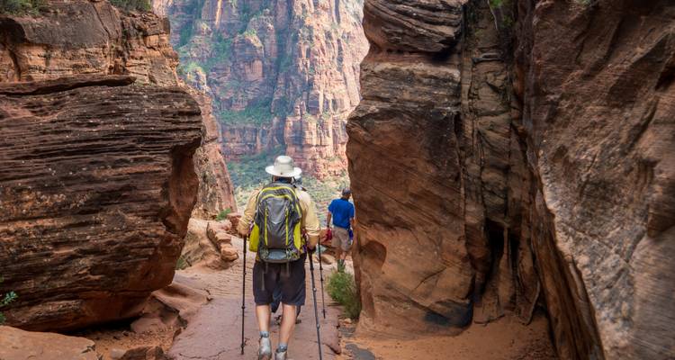 Hiker walking through narrow red rock canyon.