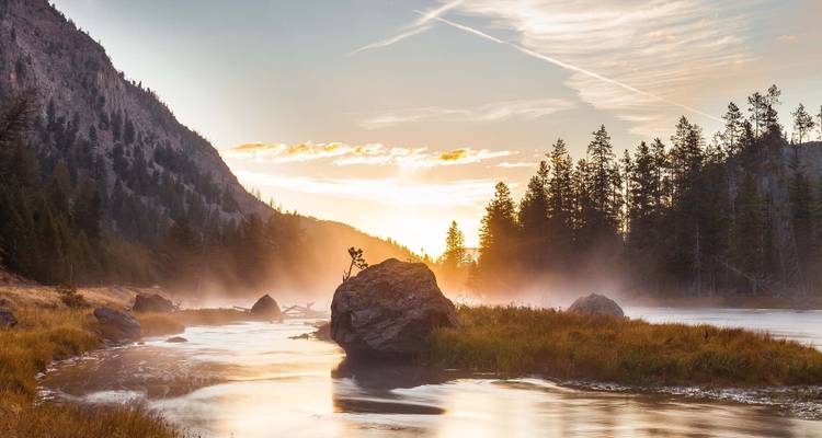 Nebelige Flusslandschaft bei Sonnenaufgang mit bewaldeten Hügeln.