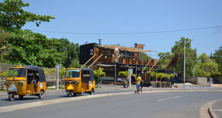 Straatbeeld met tuk-tuks en een modern gebouw.