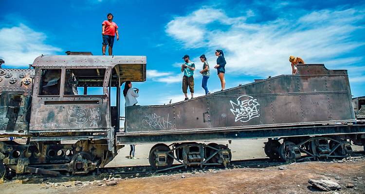 Reizigers klimmen en verkennen de roestige romp van een oude locomotief in Boliviƒs afgelegen woestijnspoorwegbegraafplaats.