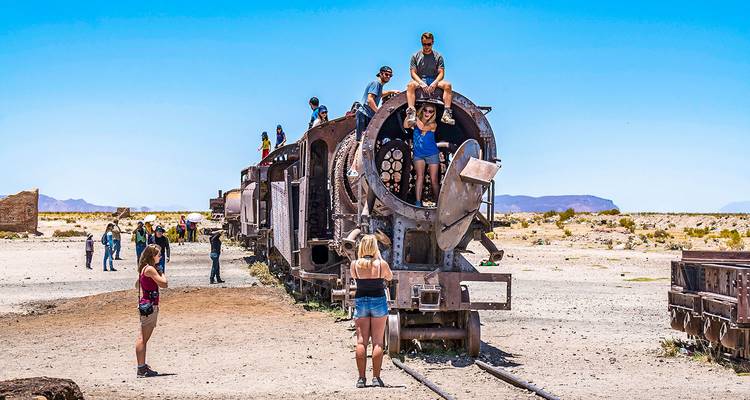 Les touristes posent à l'intérieur et sur la partie cylindrique avant d'une locomotive à vapeur abandonnée dans le désert bolivien.