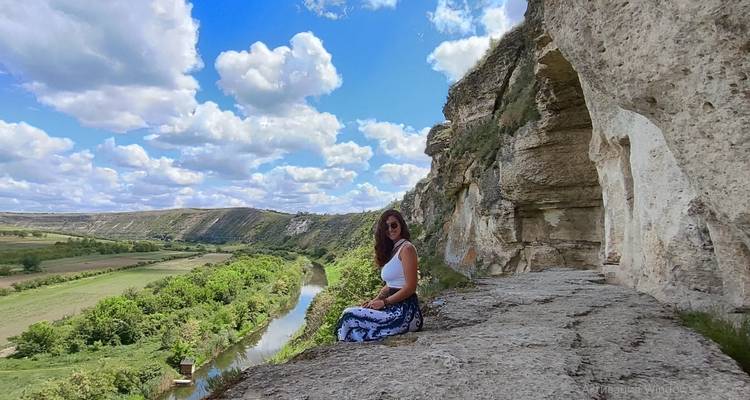 Vrouw zittend op kalkstenen klif met uitzicht op een kronkelende rivier en lapwerk Moldavisch platteland onder pluizige wolken.