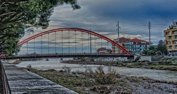 Rode gewelfde brug over een rivier met gebouwen aan de rivieroever.