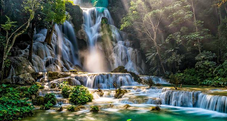 Waterfall surrounded by lush greenery with sunlight streaming through.