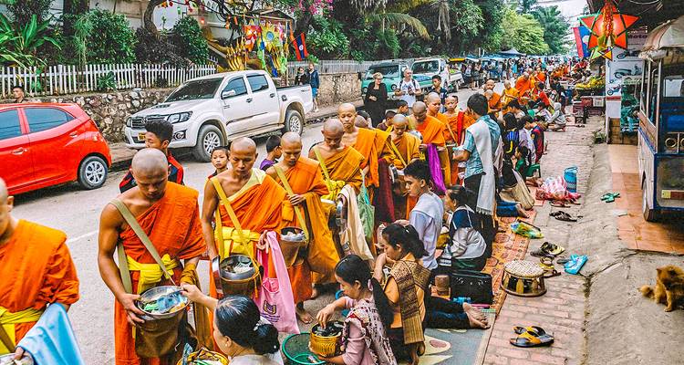 Monks in orange robes walking down a street as part of a procession.