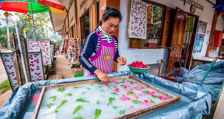 Woman crafting with flowers and leaves in a traditional setting.