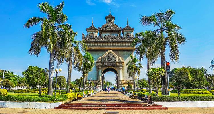 Monumental arch framed by palm trees on a sunny day.