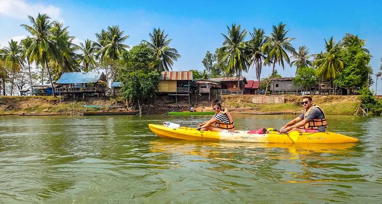Two people kayaking on a river surrounded by traditional houses.