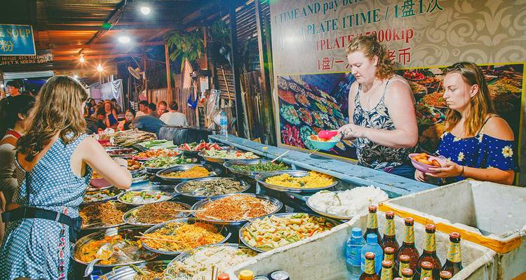 People selecting food from a variety of dishes at a night market.