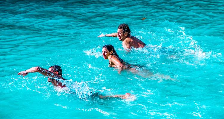 Three people swimming energetically in clear blue water.