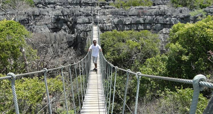 Man die over een touwbrug loopt boven rotsachtig terrein.