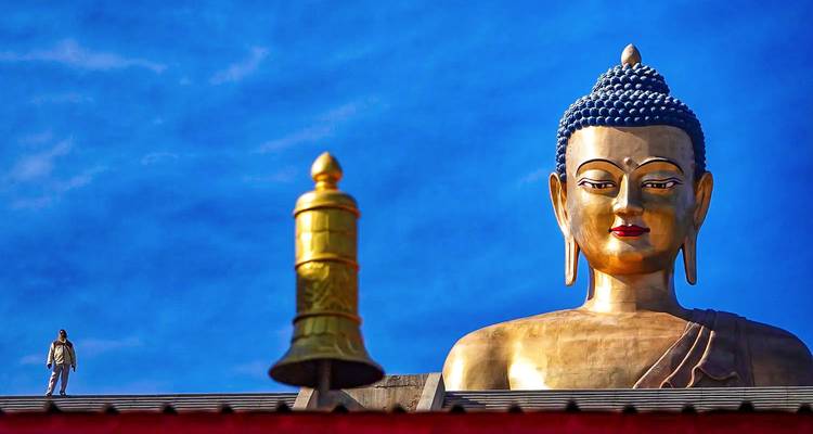 Gran estatua de Buda con cielo azul y una campana en primer plano.