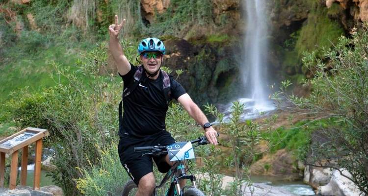 Un homme sur un vélo faisant un signe de paix devant une cascade.