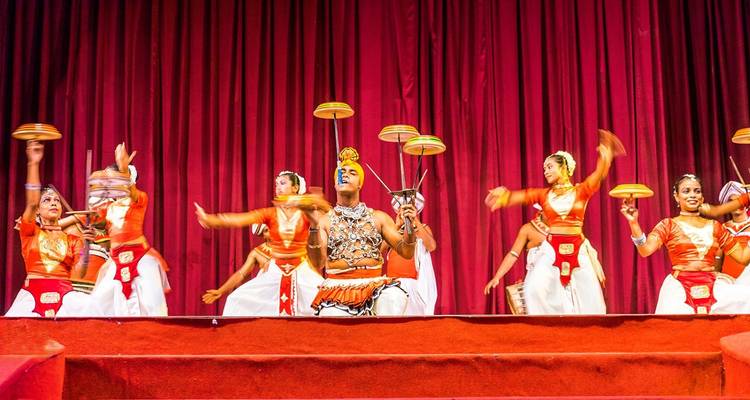 Traditional Kandyan dancers in bright costumes perform with spinning plates on stage.