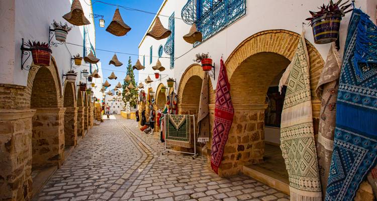 Charmante Kopfsteinpflastergasse gesäumt von Bögen, gewebten Teppichen und hängenden Korblampen in einer tunesischen Medina.