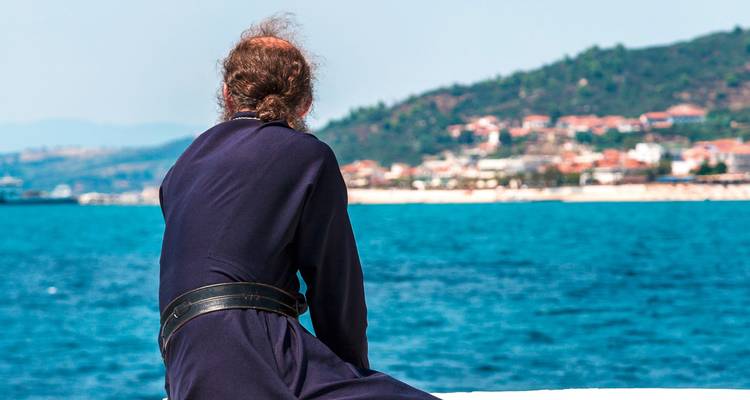 A man sitting by the sea overlooking a coastal town.