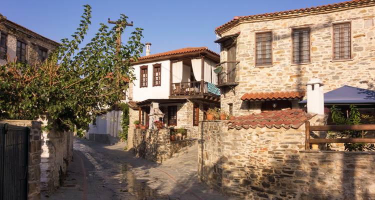 Malerische Steingasse mit traditionellen mazedonischen Häusern und Ziegeldächern unter blauem Himmel.