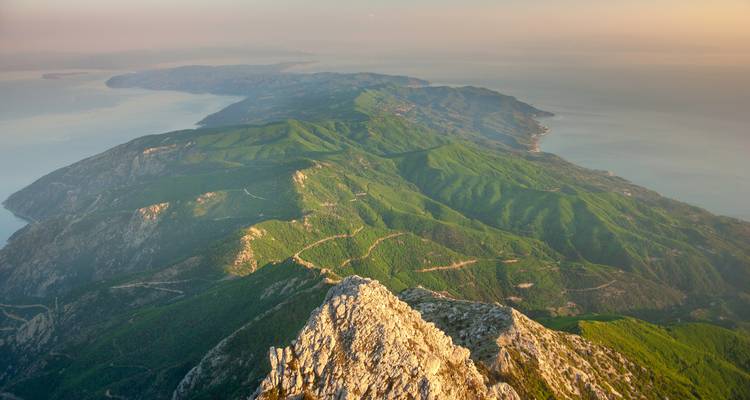 Raue Luftaufnahme einer bewaldeten Halbinsel und des umgebenden Meeres, gesehen vom Berggipfel.